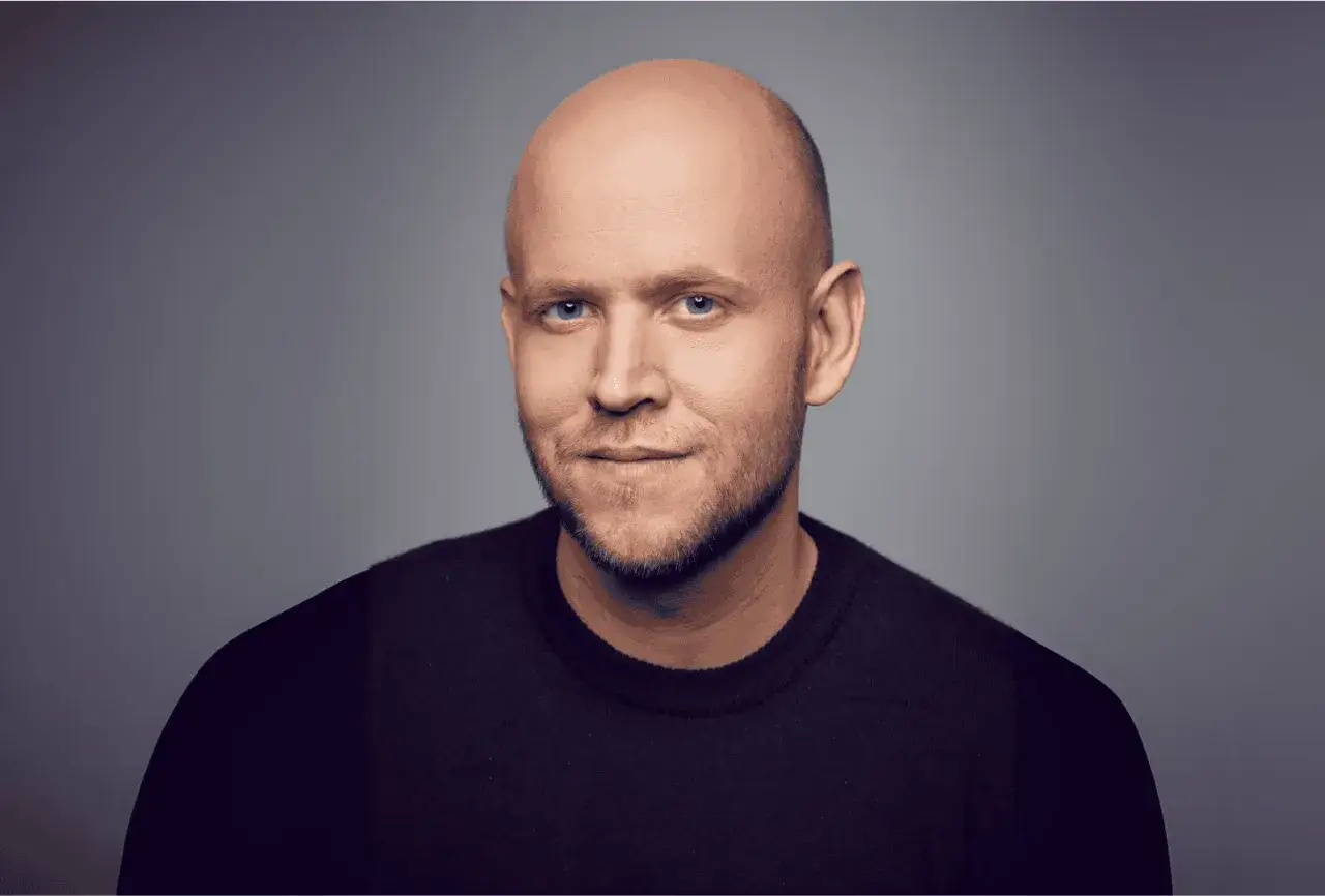 Daniel Ek, grundare av Spotify, med bl&aring; &ouml;gon och sk&auml;ggstubb, b&auml;r en svart tr&ouml;ja mot en gr&aring; bakgrund.