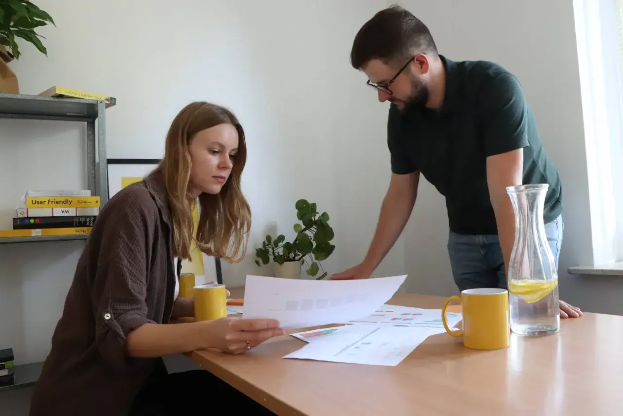 UX researcher analizuje dokumenty z kolegą przy biurku.