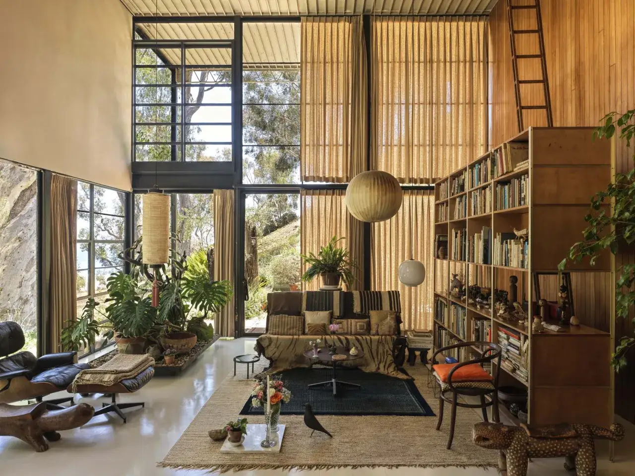 Interno della Eames House con mobili iconici, piante rigogliose e ampie finestre che incorniciano il paesaggio.