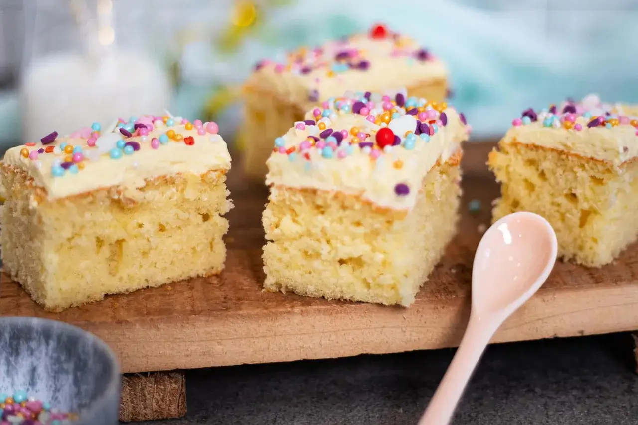Vier Stücke saftiger konfetti kuchen mit hellem Zuckerguss und bunten Streuseln, bereit zum Genießen.