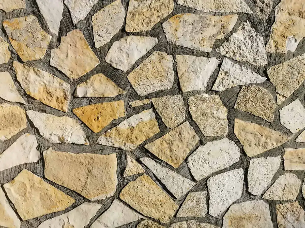 Kamień piaskowiec tworzy mozaikową ścianę. Różnorodne kształty i odcienie kamienia nadają jej naturalny, rustykalny charakter.