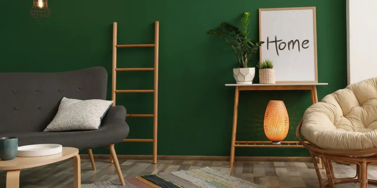 Salon cosy avec mur vert sapin. Quel couleur avec le vert sapin ? Le gris du canapé, le beige du fauteuil, et l'orange de la lampe créent une ambiance chaleureuse.