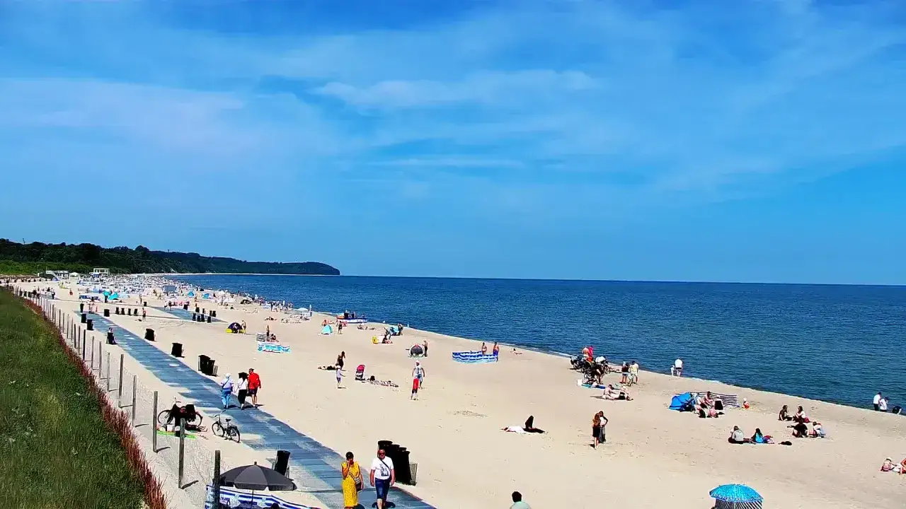 Słoneczny dzień na plaży we Władysławowie. Tłumy plażowicz&oacute;w, niebieskie morze i szeroka, piaszczysta plaża.