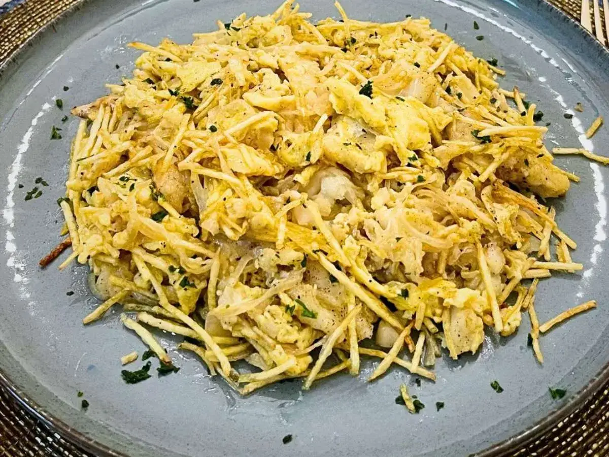 Delicioso bacalao a bras, un plato tradicional con patatas finas, huevo y perejil picado, servido en un plato gris.