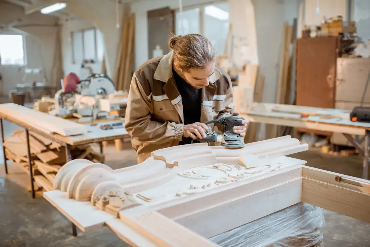 Craftsman sands a detailed wooden carving, showcasing the beauty of solid wood material in his workshop.
