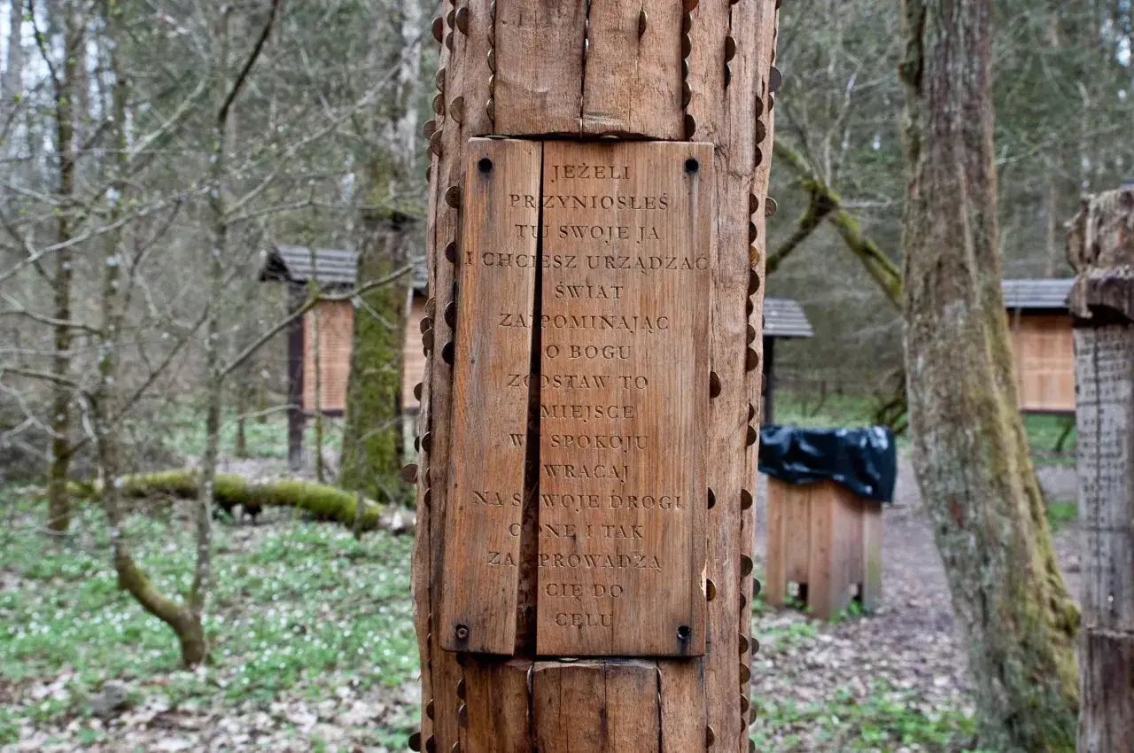 Drewniany słup z wyrytą sentencją w lesie, symbolizujący miejsce mocy Białowieża. Monety wbijane w pień drzewa.
