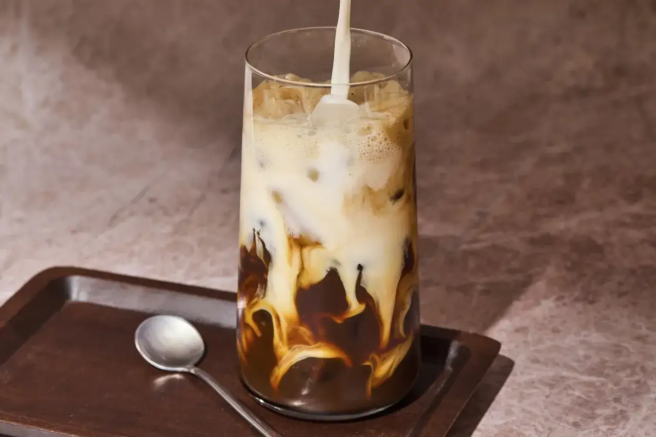 Mleko spływa po kostkach lodu, tworząc piękne wzory w szklance z espresso z lodem.