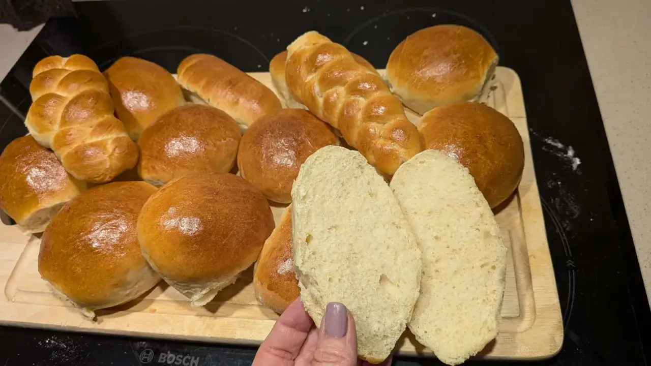 Una variedad de panes caseros, incluyendo trenzas y bollos, con dos rebanadas de pan de leche sostenidas en primer plano.