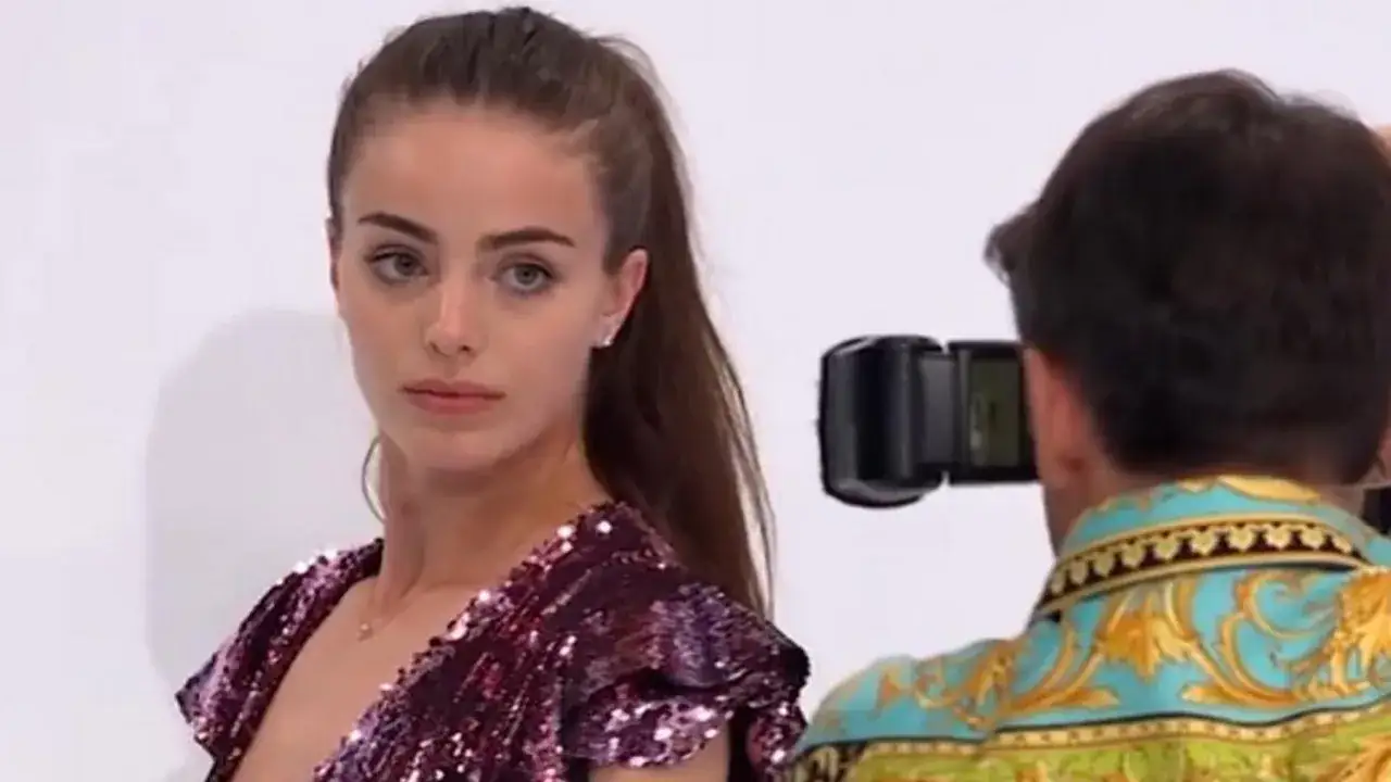 Klaudia El Dursi, top model, w błyszczącej sukience pozuje do zdjęcia. Fotograf w barwnej koszuli celuje aparatem.