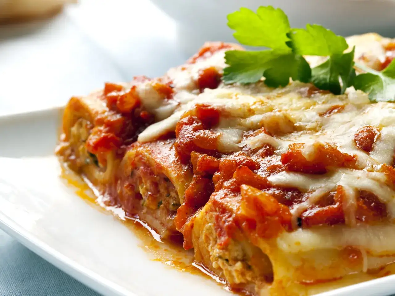 Cannelloni di carne ricetta della nonna, gustosi e filanti, con sugo rosso e formaggio fuso, guarniti con prezzemolo fresco.