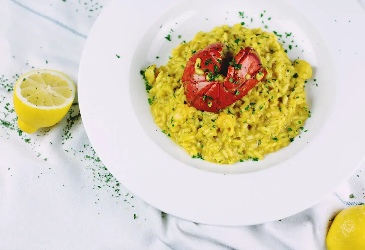 En krämig risotto med hummer, garnerad med persilja. En halv citron ligger bredvid, som en påminnelse om den italienska pastans fräscha smak.