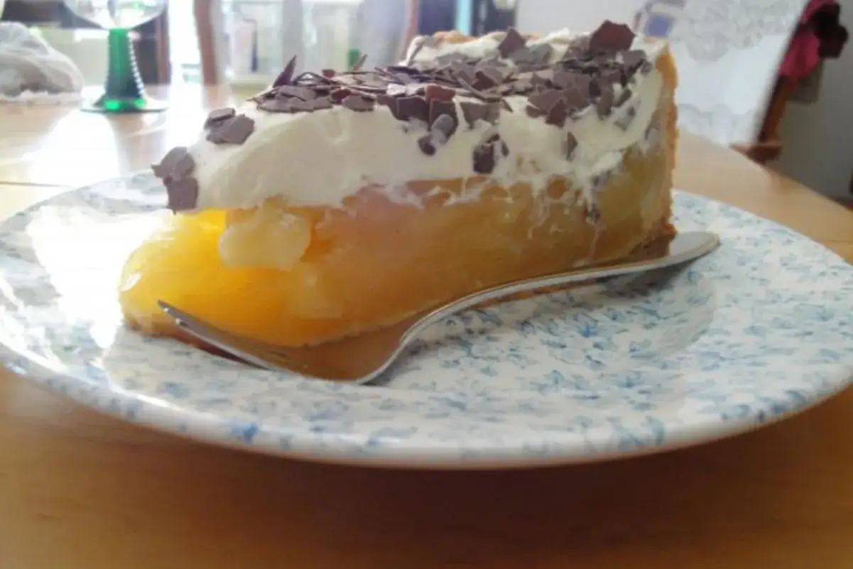 Ein Stück Apfel Sekt Torte mit Sahne und Schokostreuseln auf einem blauen Blumenteller.