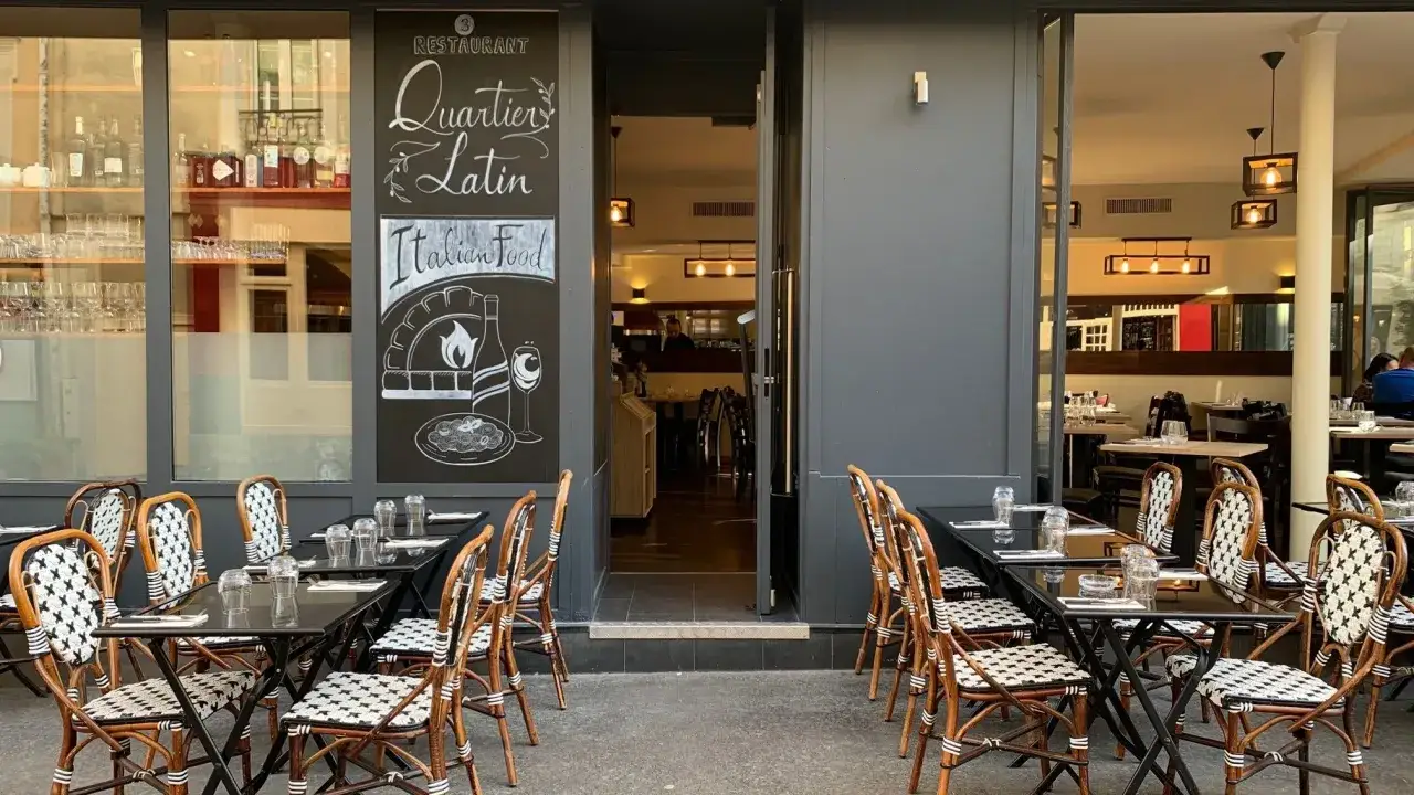 Terrasse de restaurants quartier latin. Tables dressées, chaises en rotin, et une ardoise annonçant 