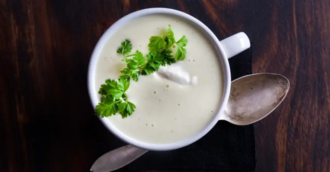 Krämig soppa med creme fraiche, garnerad med persilja, serverad med en sked på en mörk träyta.