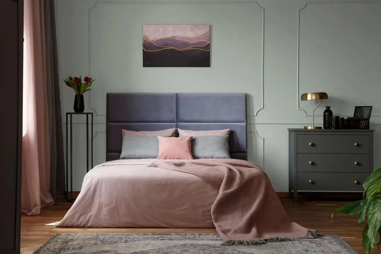 Ein Schlafzimmer mit einem beigen Bett und Kissen. Die Wandfarbe ist ein sanftes Gr&uuml;n. Welche Farbe passt zu Beige? Hier sehen wir Rosa und Grau als harmonische Erg&auml;nzung.
