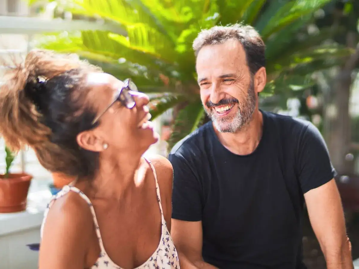 Pareja riendo al aire libre. &Eacute;l, con barba canosa, sonr&iacute;e, superando la crisis de los 50 en hombres. Ella, con gafas, se r&iacute;e a carcajadas.