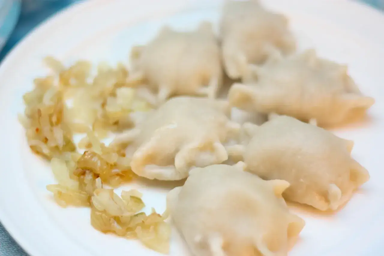 Kilka pysznych pierogów z mięsem mielonym surowym, podanych z podsmażoną cebulką na białym talerzu.