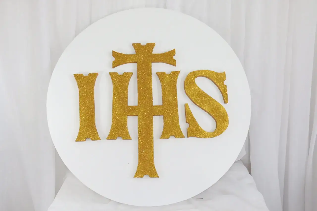 Złoty symbol IHS, oznaczający Jezusa Chrystusa, na białym tle.