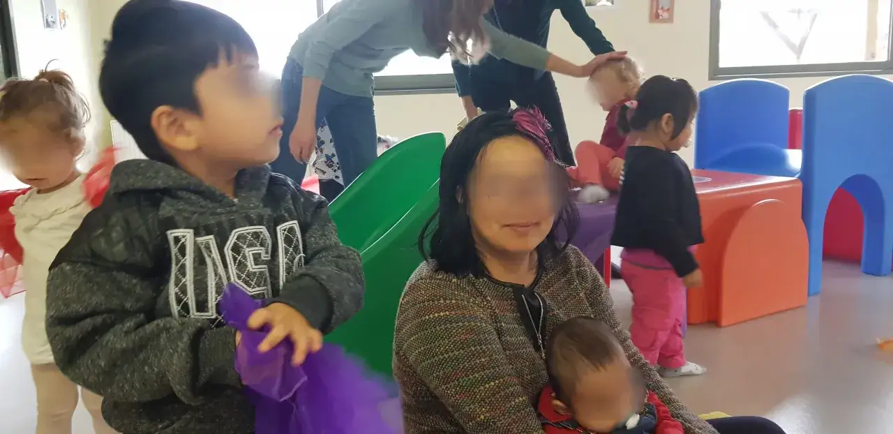 Une mère au foyer surveille ses enfants jouant dans une aire de jeux intérieure colorée.