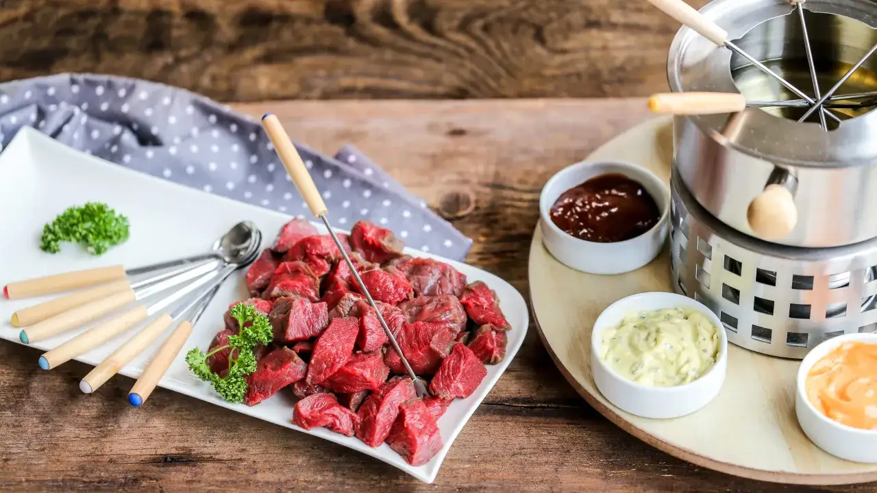 Pr&eacute;paration pour comment faire une fondue bourguignonne : cubes de b&oelig;uf cru, sauces et appareil &agrave; fondue sur table en bois.