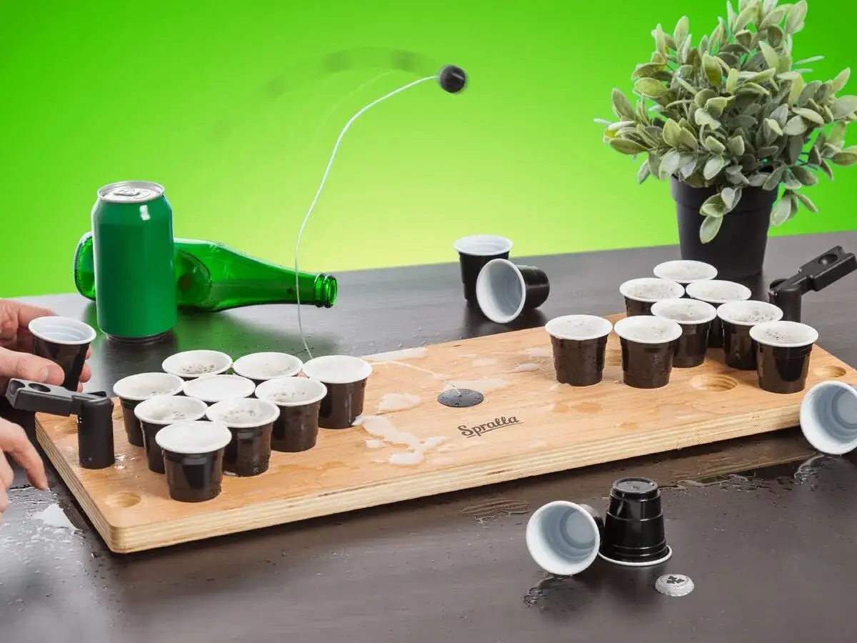 En rolig lekar fest vuxna inomhus med beer pong-spel. En boll flyger mot muggarna p&aring; tr&auml;plattan.