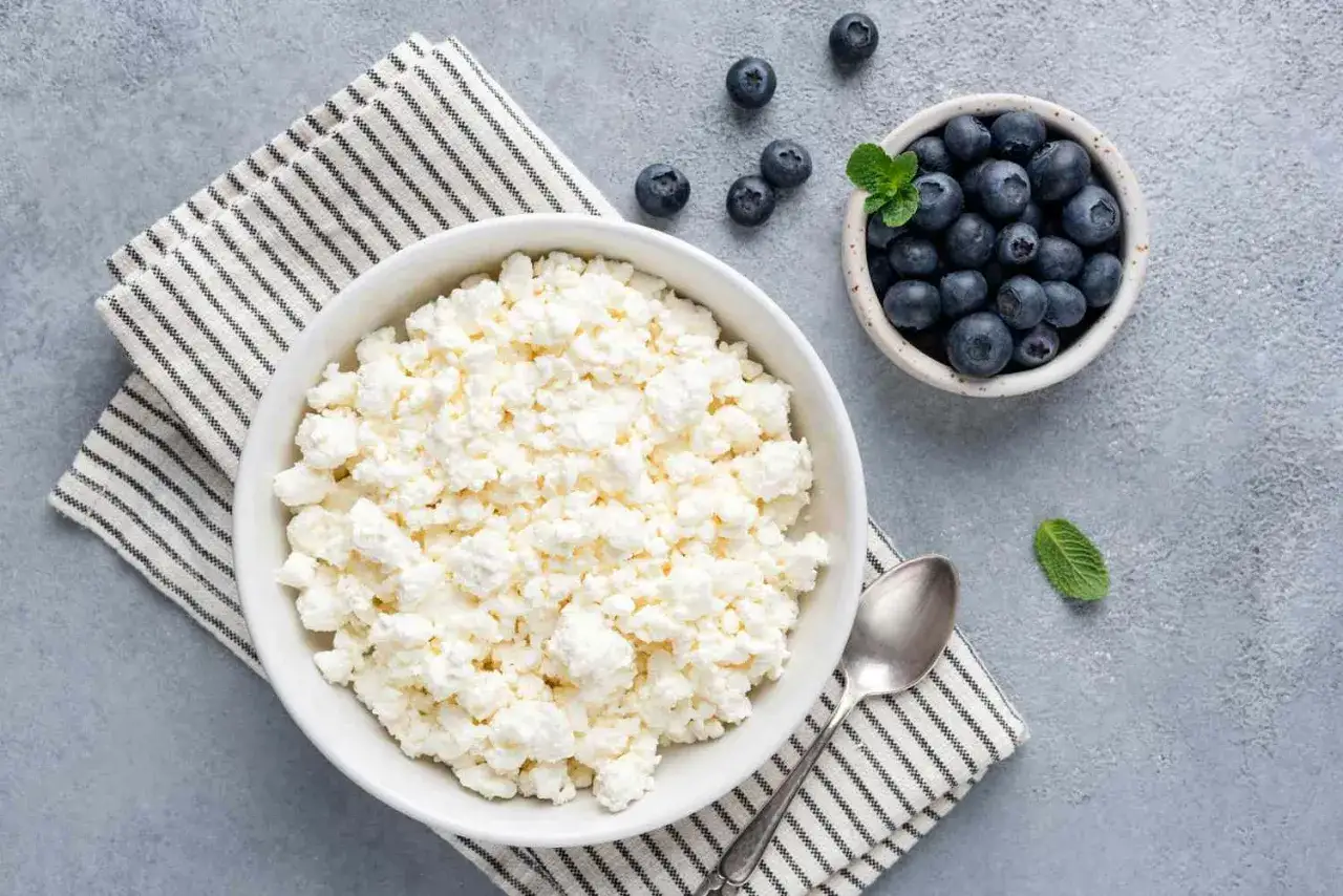 Una ciotola di fiocchi di latte, con mirtilli accanto. Attenzione, i fiocchi di latte fanno ingrassare se consumati in eccesso.