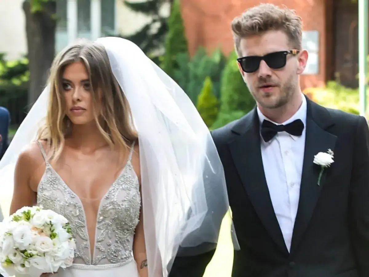 Antek Królikowski i Joanna Opozda w dniu ślubu. Panna młoda w sukni z welonem i bukietem, pan młody w garniturze i okularach.