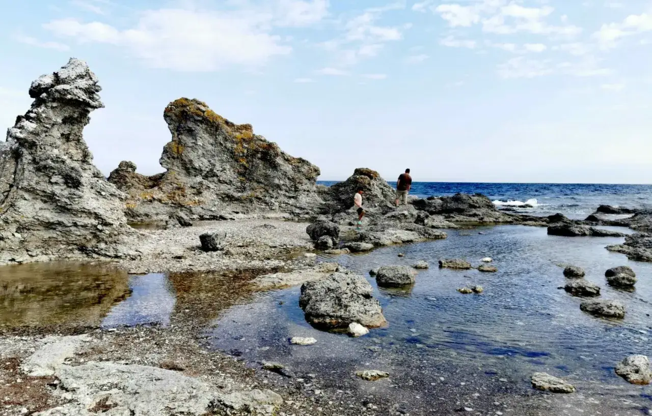 Klippformationer vid havet på Gotland i Sverige. Två personer utforskar den steniga stranden med små vattenpölar.