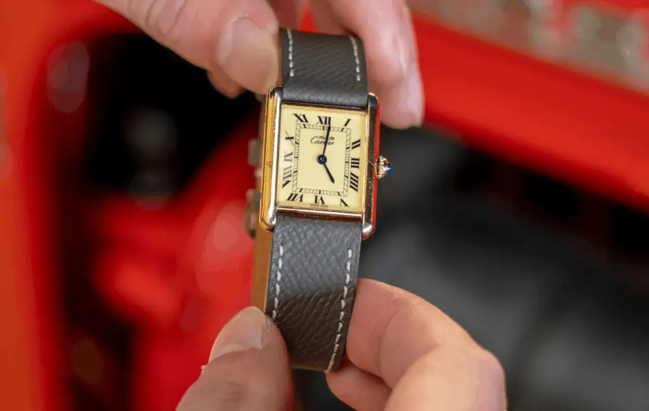 Złoty zegarek Cartier z szarym paskiem, z rzymskimi cyframi na tarczy. Mechanizm zegarka jest sercem tej eleganckiej maszyny.