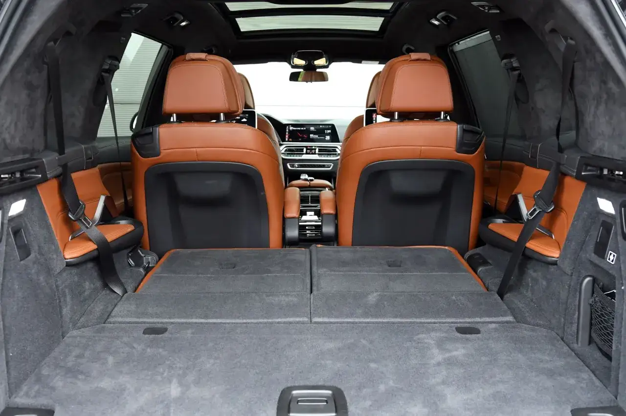 Wnętrze BMW X7 z brązową skórzaną tapicerką i rozłożonymi siedzeniami. Sprawdź wymiary BMW X7, aby zaplanować podróż.