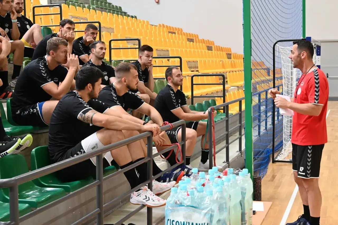 Trener Vive Kielce w czerwonej koszulce przemawia do zawodnik&oacute;w siedzących na trybunach.