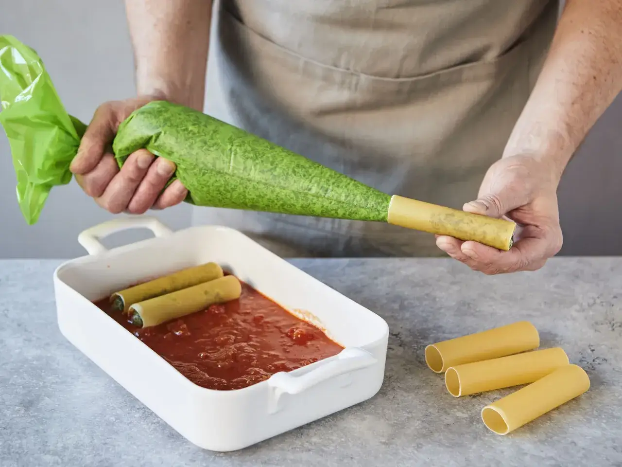 F&uuml;llen einer Cannelloni-R&ouml;hre mit gr&uuml;ner F&uuml;llung f&uuml;r ein k&ouml;stliches Cannelloni-Rezept.