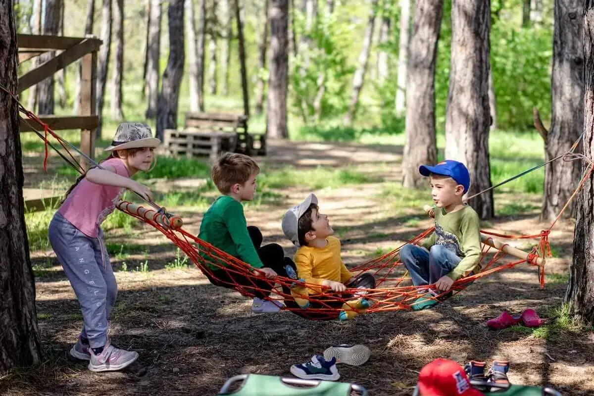 Vier Kinder, darunter ein Kind 8 Jahre, sitzen in einer Hängematte im Wald.