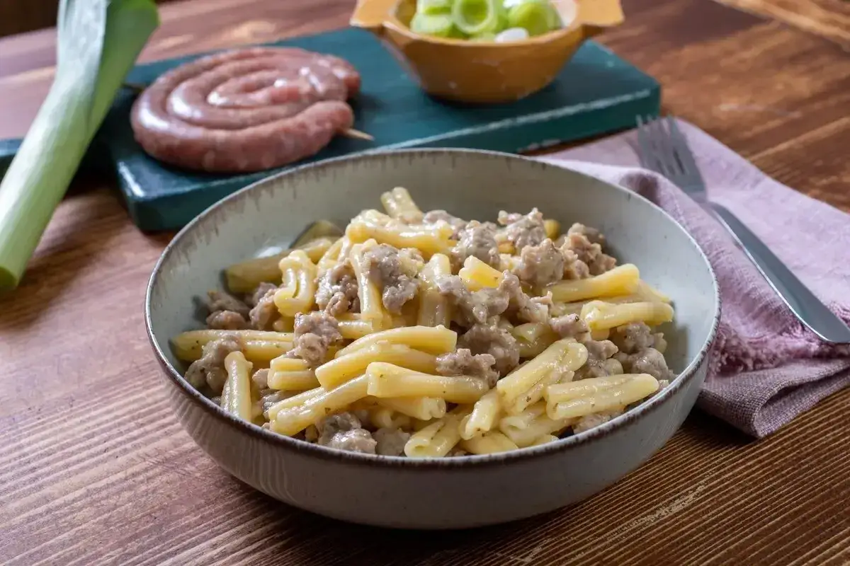 Un piatto invitante di pasta porri e salsiccia, con ingredienti freschi sullo sfondo.