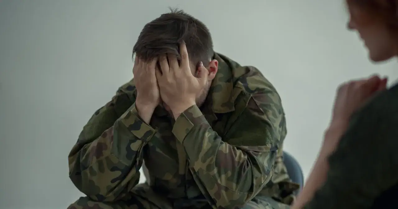 Żołnierz w mundurze z kamuflażem, z rękami na twarzy, przechodzi trudne testy psychologiczne do wojska.
