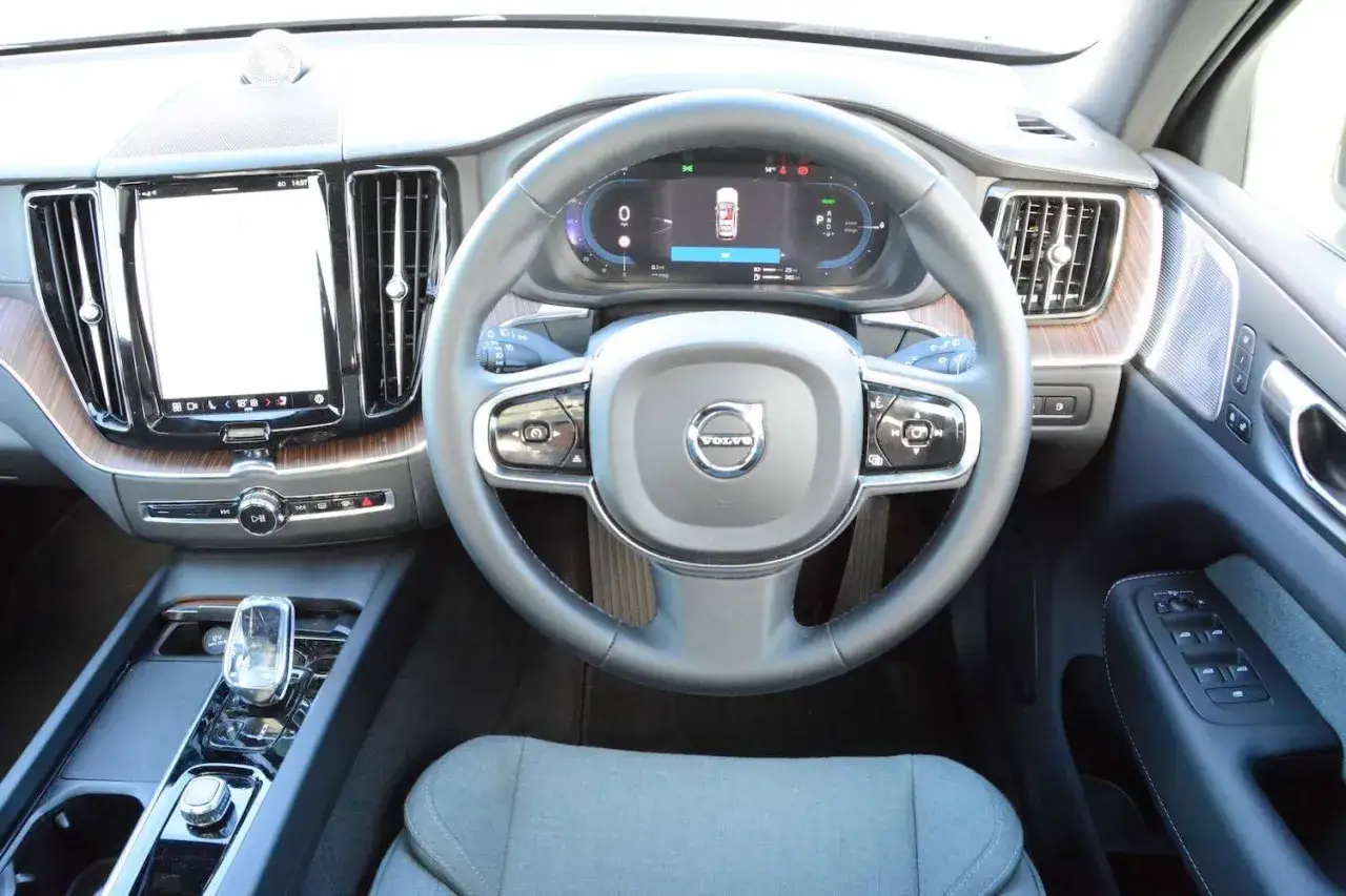 Wnętrze Volvo XC60 T6: kierownica, cyfrowy kokpit, ekran multimediów i eleganckie drewniane wykończenie.