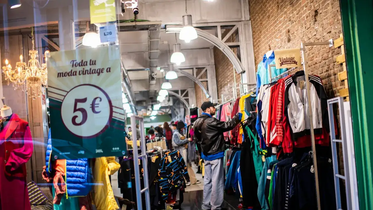 Un hombre busca ropa vintage en una tienda. Un cartel anuncia 