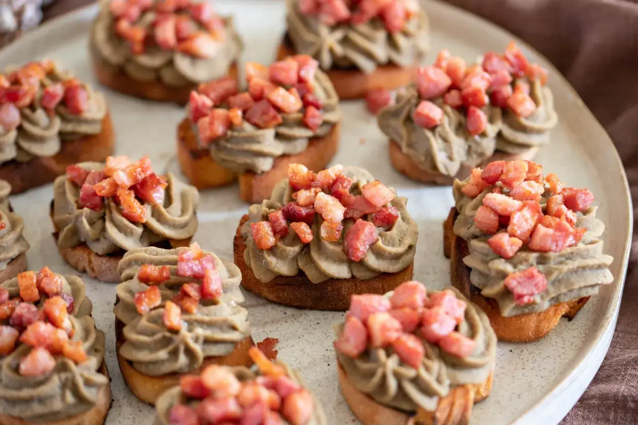 Deliziosi crostini con pat&eacute; di lenticchie e cubetti croccanti di pancetta. Un antipasto perfetto per ogni occasione.