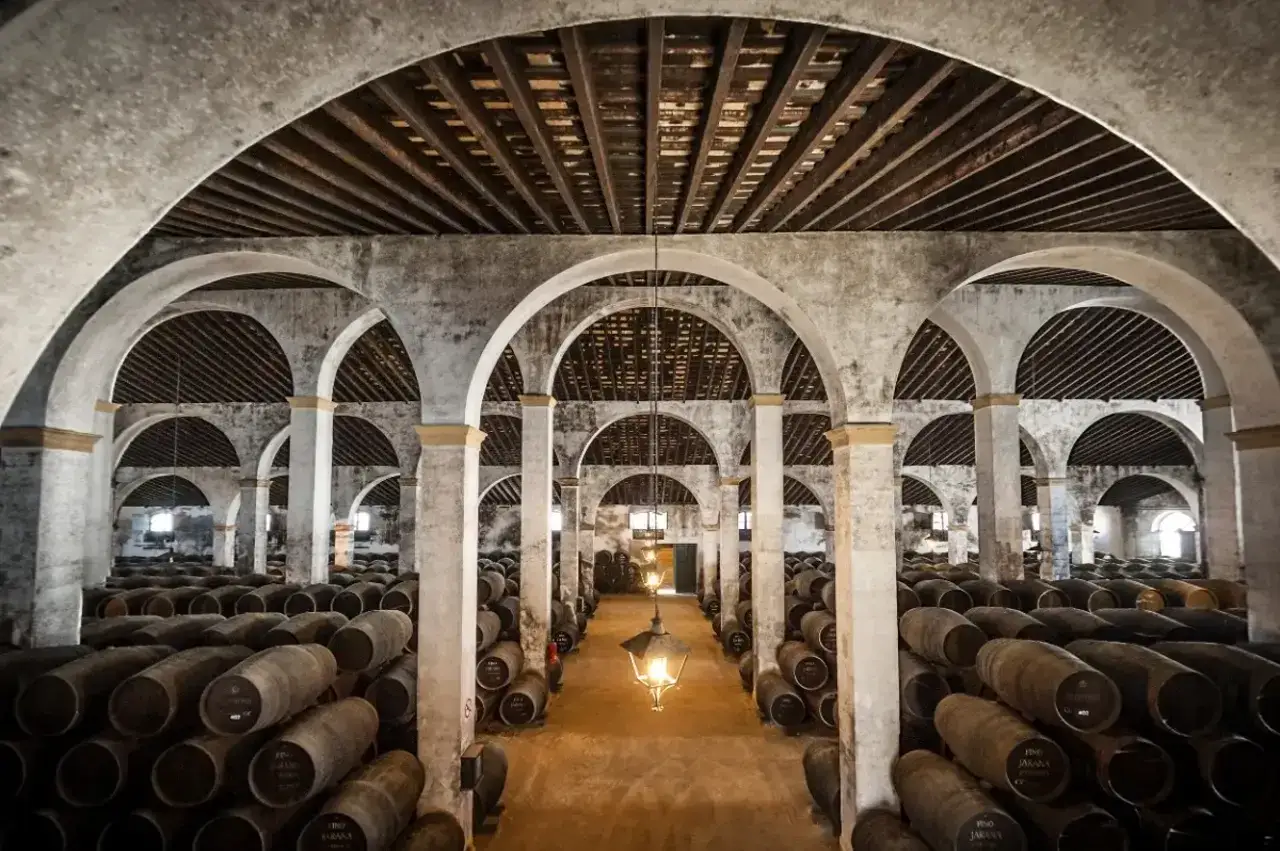 Bodega en Jerez de la Frontera, con hileras de barricas de roble bajo arcos de piedra. Un lugar imprescindible que ver en Jerez de la Frontera en un día.