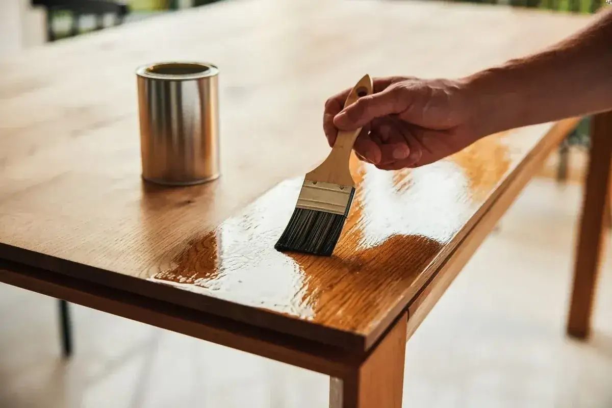 Main d'une personne appliquant du vernis sur une table en bois pour la customiser et la relooker.