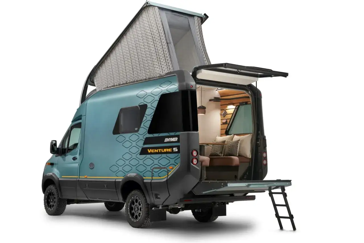 Hymer Venture S z podniesionym dachem i otwartym tyłem, ukazując przytulne wnętrze z kanapą i poduszkami.