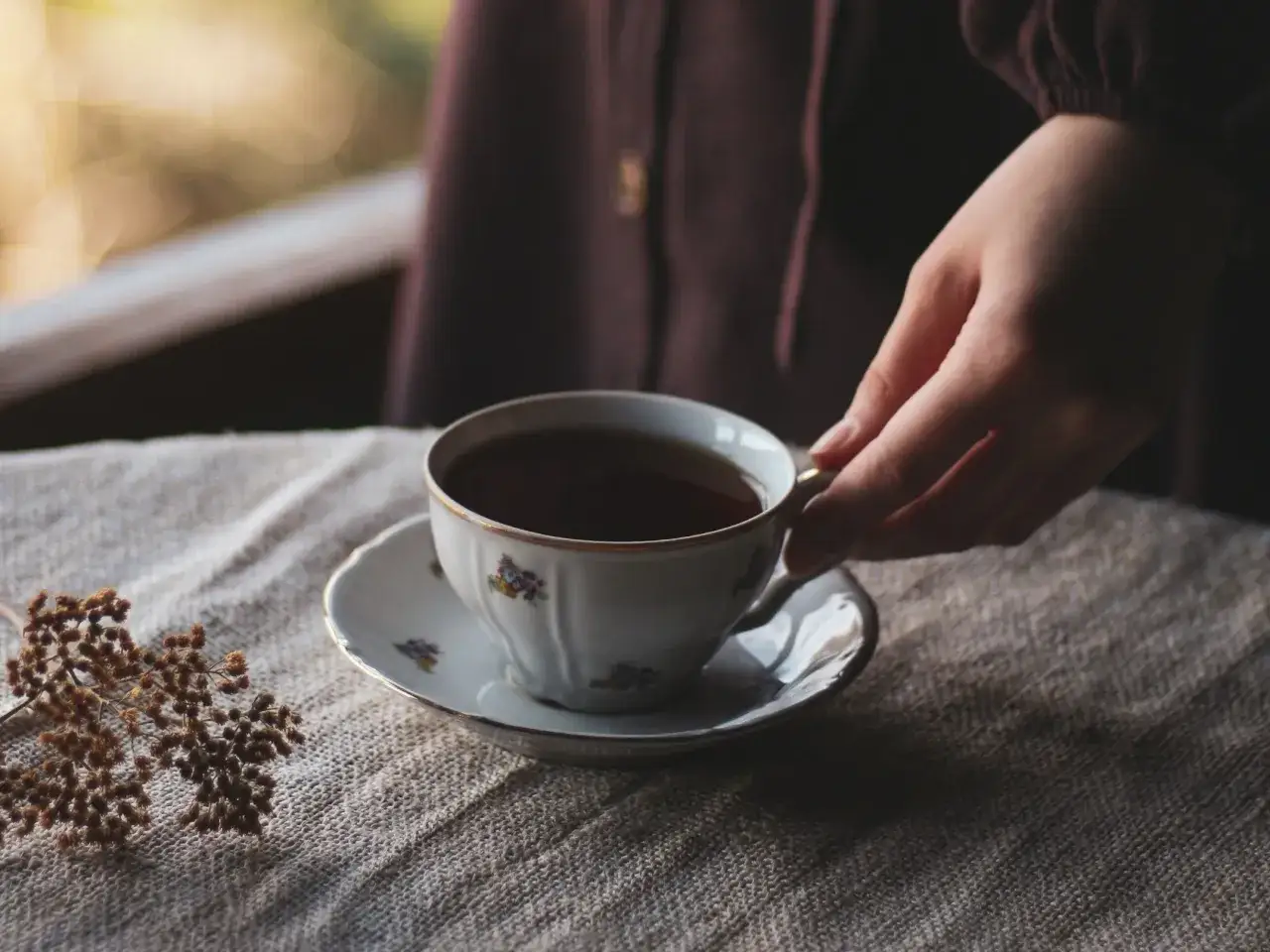 Une main saisit une tasse de th&eacute; orn&eacute;e de fleurs, un moment de qui&eacute;tude qui c&eacute;l&egrave;bre la culture du th&eacute;.