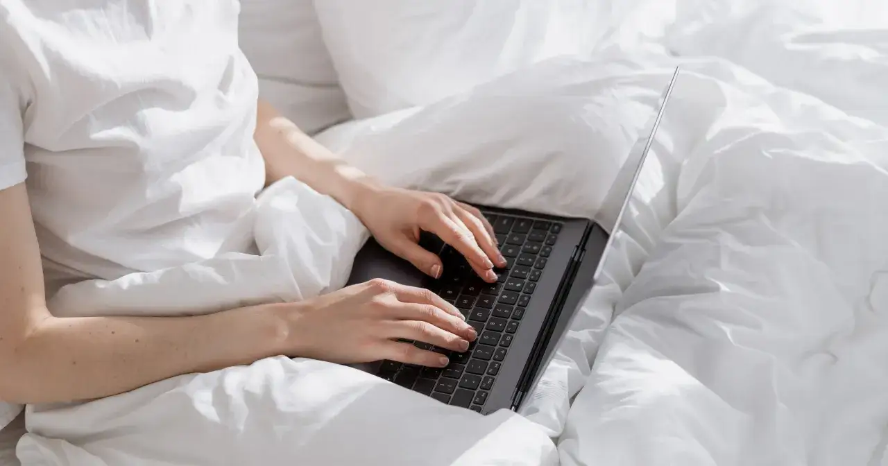 Osoba w białej koszulce pracuje na laptopie w łóżku. Zastanawia się, czy premia wlicza się do L4.