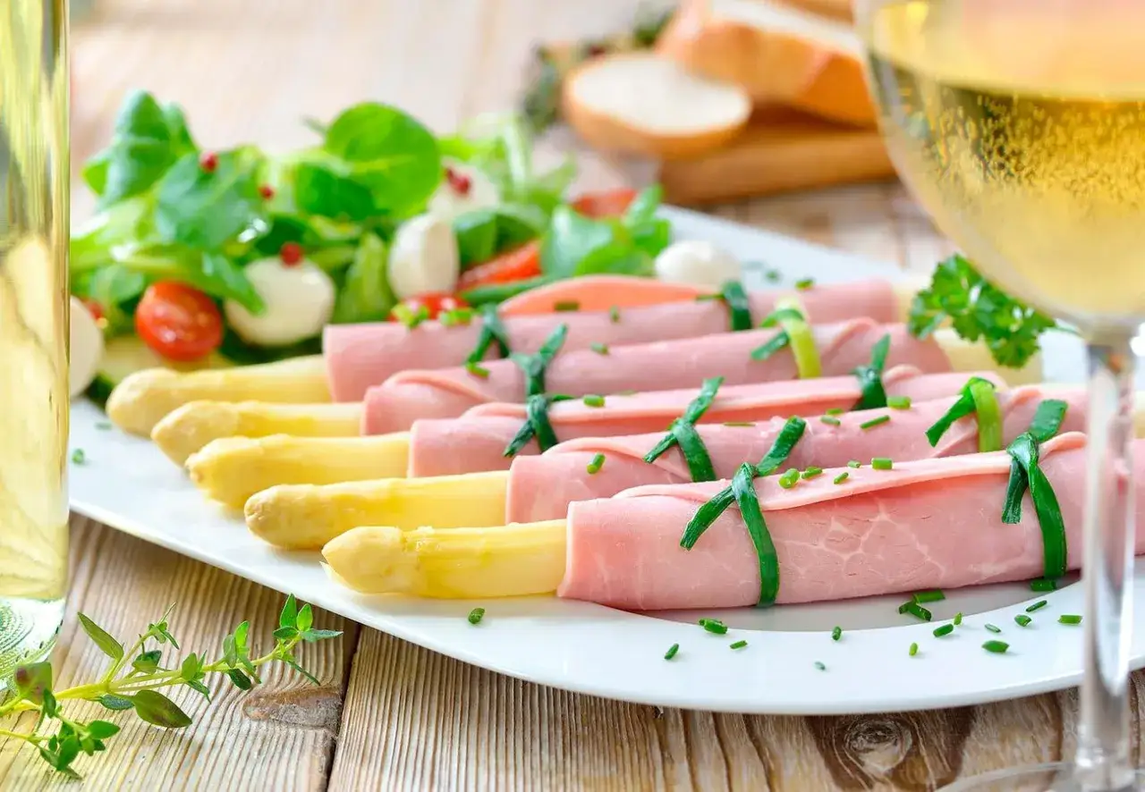 Rollitos de jam&oacute;n york envuelven esp&aacute;rragos blancos, servidos con ensalada y pan. Un aperitivo ligero y delicioso.