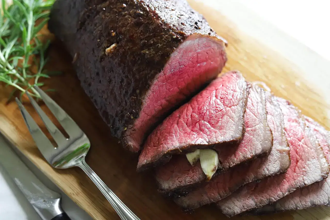 Un rôti de bœuf saignant, tranché, avec des gousses d'ail et du romarin. Une recette de rond de Paris parfaite pour un repas festif.