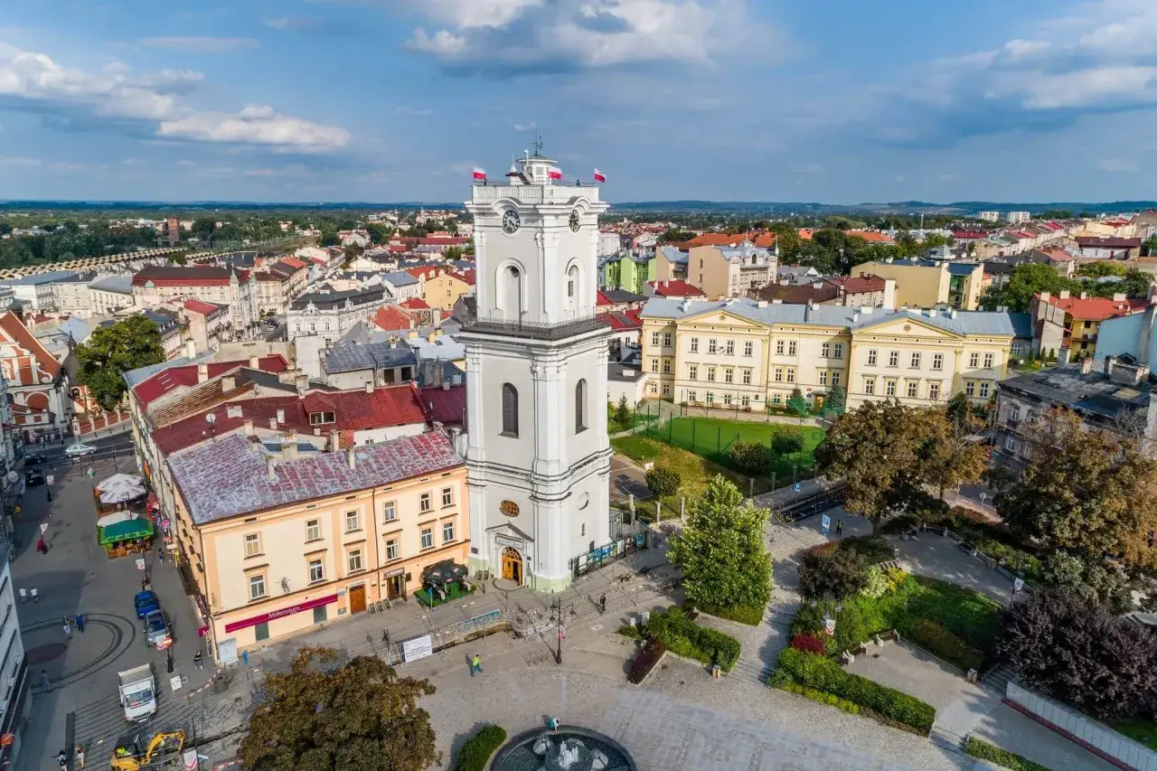 Wieża ratuszowa w centrum miasta, otoczona kamienicami i zielenią. Warto przemyśl atrakcje tego miejsca.