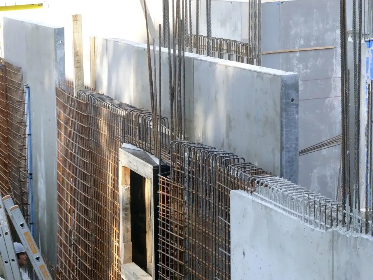 Betonw&auml;nde und Bewehrungsstahl f&uuml;r eine STB Decke. Ein Bauarbeiter schaut hinter einer Leiter hervor.