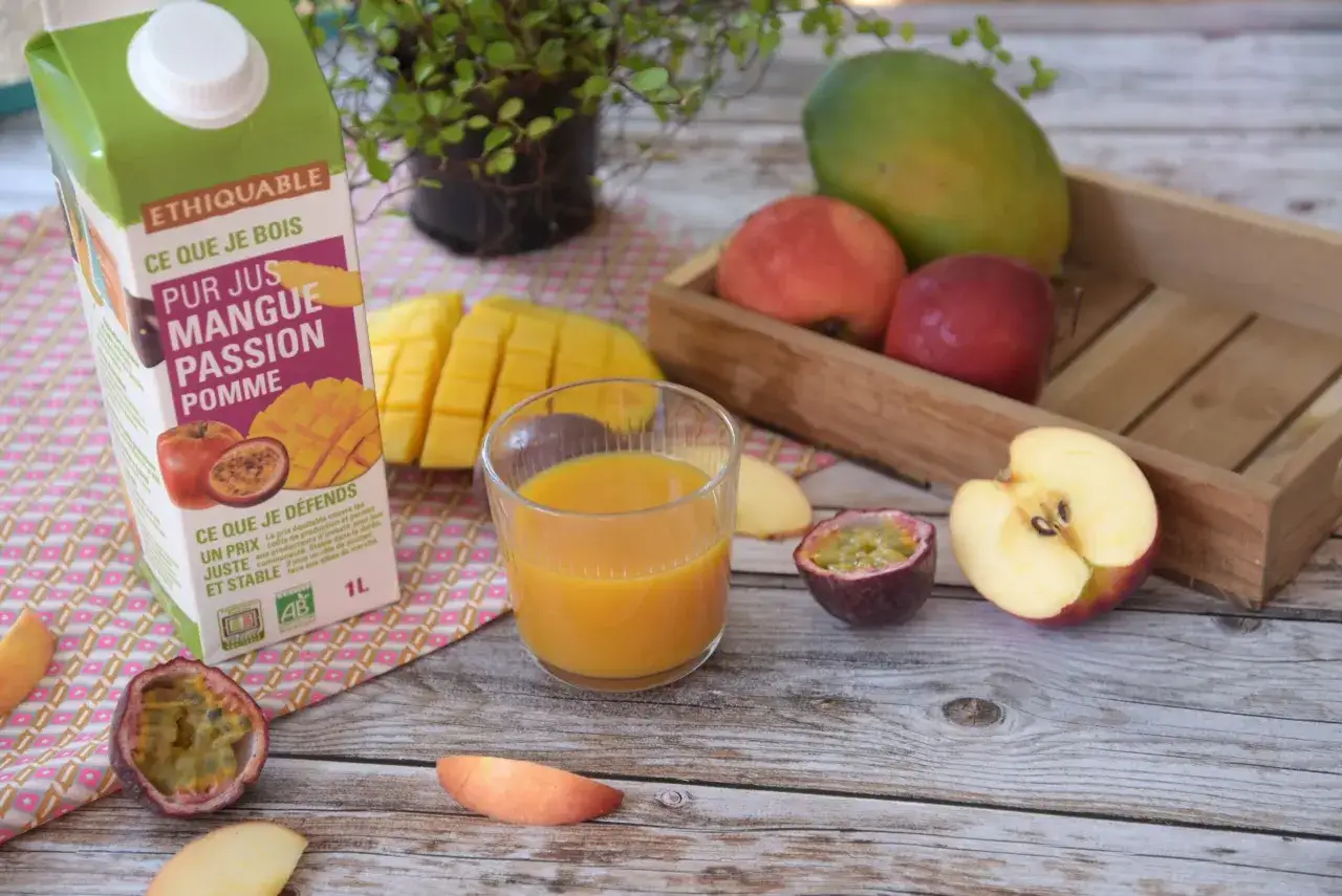 Un verre de jus mangue-passion-pomme, le meilleur jus de fruit, à côté de fruits frais et d'une brique de jus.