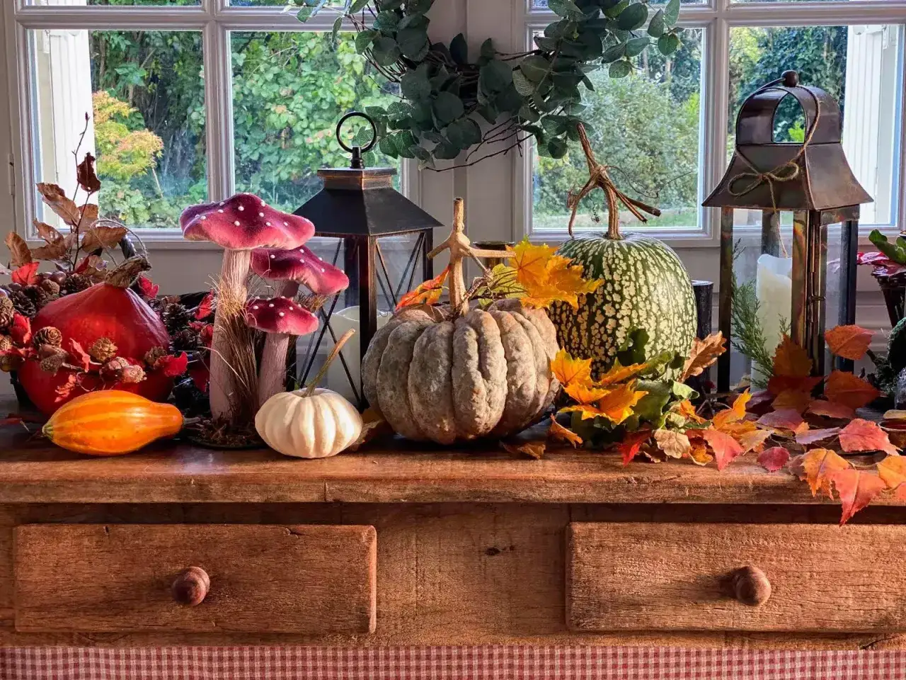 D&eacute;coration d'automne avec citrouilles, champignons, lanternes et une **feuille morte** aux couleurs vives sur un buffet en bois.
