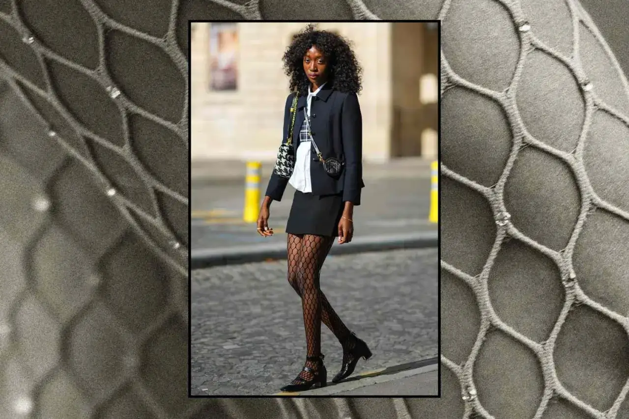 Une femme porte une jupe noire, un blazer et une chemise blanche, complétés par des collants résille. Une idée tenue chic et audacieuse.